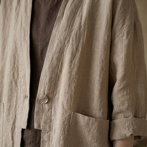 Pu&ograve; includere: Giacca in lino beige dalla vestibilit&agrave; morbida, con chiusura a un solo bottone e due tasche frontali. Le maniche sono arrotolate e la giacca &egrave; sovrapposta a un top marrone. Il tessuto ha un aspetto strutturato.