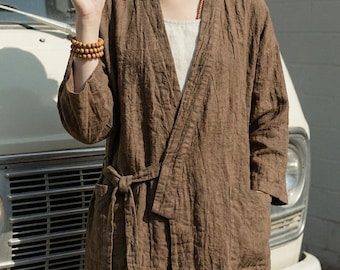 May include: A brown open-front jacket with three-quarter length sleeves, a tie-waist closure, and two front patch pockets. The garment features a textured fabric finish and is worn over a light-colored, plain, sleeveless undergarment.