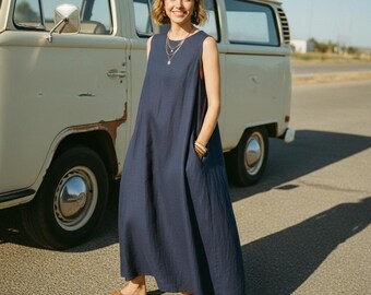 May include: A sleeveless, navy blue maxi dress with pockets. The dress is worn with woven brown sandals and layered gold necklaces. A vintage cream-colored van is in the background.