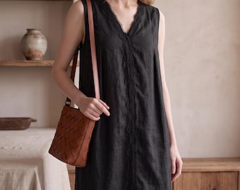 May include: A sleeveless black midi dress featuring a V-neckline with delicate black lace trim and a vertical lace panel down the center. The dress is paired with a brown leather crossbody bag that has a woven, textured surface pattern.