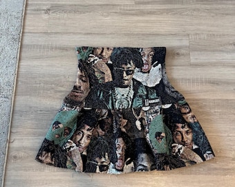 May include: A woven mini skirt with a collage of faces in green, black, and brown. The skirt has a flared shape and a textured appearance. The word "EERBCIST" is visible on the skirt.