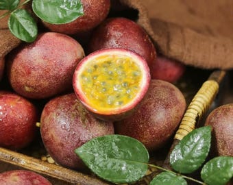 May include: A close-up shot of several passion fruits, some whole and others cut open to reveal the yellow pulp and seeds. The fruits are a deep reddish-purple color, with green leaves and stems scattered around them. The image is well-lit and shows the texture of the fruit.