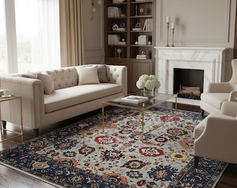 May include: A living room with a patterned rug as the focal point. The rug has a navy blue border and a central design with red, yellow, and blue floral motifs. A beige sofa, armchairs, and a fireplace are also visible in the room.