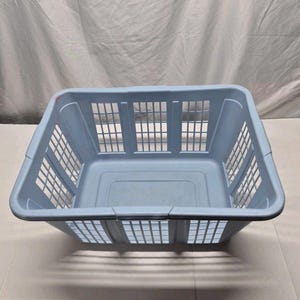 Puede incluir: Una cesta de lavandería cuadrada de color azul claro. Los lados y la parte superior presentan un patrón de rejilla. Fabricada en plástico duradero, la cesta tiene un diseño sencillo y funcional. La cesta está vacía y lista para usar.