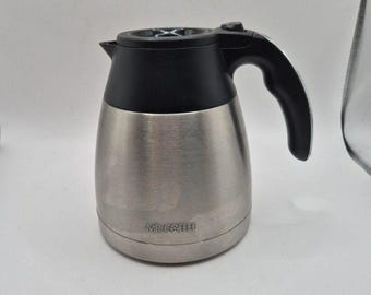 Könnte beinhalten: Eine Kaffeekanne aus Edelstahl mit einem schwarzen Kunststoffdeckel und Griff. Die Kanne hat einen abgerundeten Körper mit einer gebürsteten Metalloberfläche und dem Schriftzug MR. COFFEE in kleinen schwarzen Buchstaben auf der unteren Vorderseite.