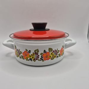 Peut inclure: Une marmite en émail blanc avec deux poignées latérales et un couvercle rouge assorti doté d'un bouton noir. L'extérieur de la marmite est décoré d'un motif floral répétitif dans des tons orange, jaune, marron et vert sur le pourtour.