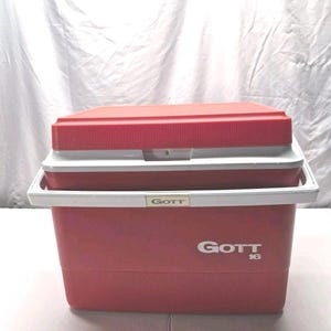 May include: A red Gott 16 cooler with a white handle and lid. The cooler has a rectangular shape with a ridged texture on the sides. The Gott logo is visible on the front and the lid is slightly ajar.
