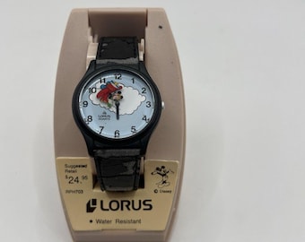 Könnte beinhalten: Eine Lorus Quarzuhr mit schwarzem Gehäuse und gemustertem schwarzem Armband. Das Zifferblatt hat einen hellblauen Hintergrund mit einer Grafik einer Figur in einem roten Flugzeug, die durch weiße Wolken fliegt, sowie schwarzen Ziffern.