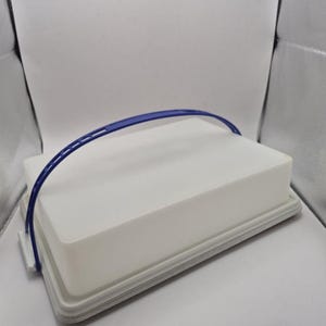 Op de afbeelding: Een witte rechthoekige voedselcontainer met een blauwe handgreep. De container heeft een deksel en een grijze rand. De handgreep loopt over de bovenkant van de container en biedt een manier om hem te dragen.