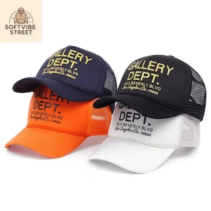 Pode incluir: Quatro bonés trucker com parte traseira em rede e frente em espuma. Os bonés estão disponíveis em azul marinho, laranja, preto e branco. Cada boné apresenta o texto GALLERY DEPT. 7613 BEVERLY BLVD Los Angeles Ca. 90036 no painel frontal.