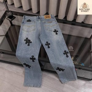 May include: Light blue denim jeans with black cross appliques. The jeans have a classic five-pocket design and a straight leg fit. The back features a leather patch. The brand name "SOFTVIBE STREET" is visible in the upper right corner.