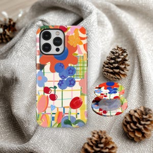 May include: A colorful phone case and matching phone grip featuring a floral and fruit pattern. The design includes blueberries, cherries, and tulips on a white grid background. The phone case is shown with a phone in it.