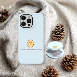 May include: A light blue phone case and matching pop socket featuring a cartoon chick with the text "Peace was never an option." The phone case has a black camera ring. Two pinecones are in the background.