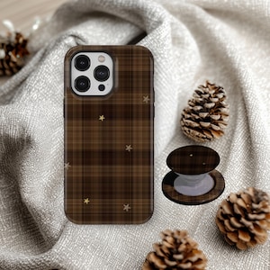 May include: A brown plaid phone case with small gold star accents and a matching circular collapsible phone grip. The case features a camera cutout with three lenses and a flash, displaying a consistent dark brown and black checkered pattern.
