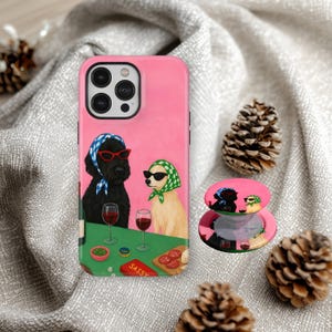 Peut inclure: Coque de téléphone rose et pop socket assorti avec une illustration amusante de deux chiens portant des lunettes de soleil et des foulards, buvant du vin. Le mot "SASSY" est sur un petit panneau. Des pommes de pin sont en arrière-plan.