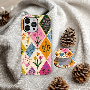 May include: A smartphone case and a matching circular phone grip featuring a diamond-patterned design filled with colourful botanical illustrations of various flowers and plants in shades of pink, yellow, orange, blue, and green on a cream background.