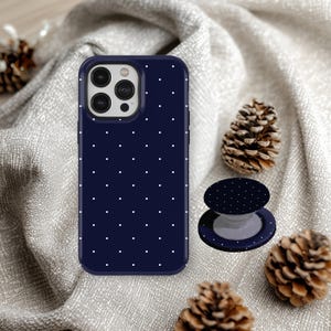 May include: Navy blue phone case and matching pop socket with a white polka dot pattern. The phone case is shown with a triple-lens camera. The pop socket is in the open position. The background includes pinecones.