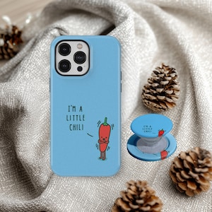 Könnte beinhalten: Eine hellblaue Handyhülle und ein passender Pop-Socket mit einem Cartoon-Chili-Pfeffer-Design. Der Text "I'M A LITTLE CHILI" ist auf beiden Artikeln aufgedruckt. Die Handyhülle hat einen schwarzen Kamerarand.