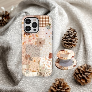 Peut inclure: Une coque de téléphone et un support assorti avec des motifs floraux et géométriques dans des tons beige, marron et crème. La coque est posée sur un tissu gris avec des pommes de pin.