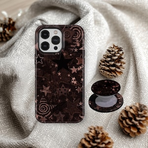 Peut inclure: Une coque de smartphone marron foncé et un support de téléphone circulaire rétractable assorti, tous deux arborant un motif répétitif d'étoiles variées et de spirales dans des tons marron et cuivre, présentés ensemble en ensemble.