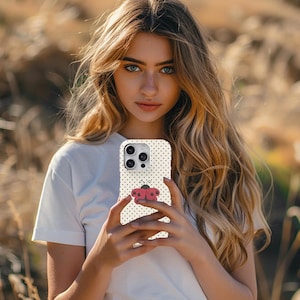 May include: A white phone case with black polka dots and a red ladybug design. The case is held in front of a person. The ladybug has a black head and red wings. The background is blurred.