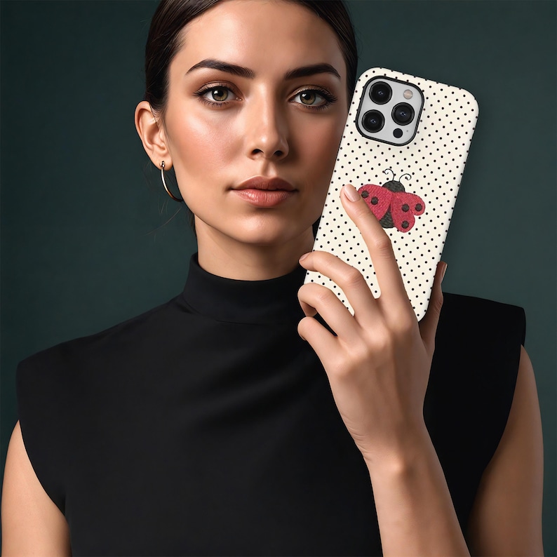 May include: A smartphone case featuring a ladybug design. The case has a cream background with black polka dots and a red and black ladybug illustration. The phone case is held by a person wearing a black top.