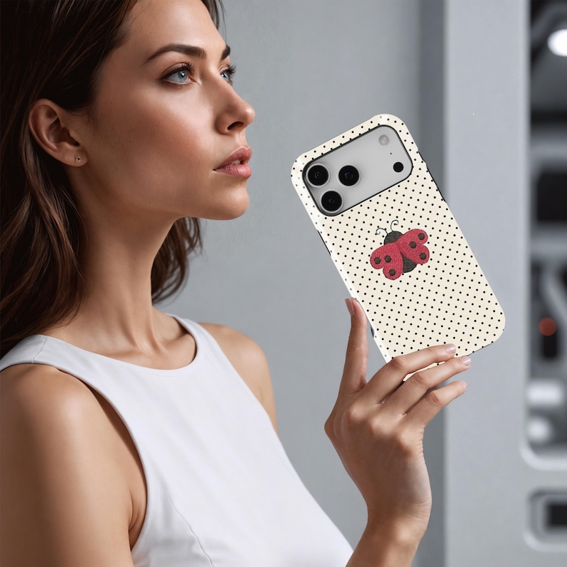 May include: A smartphone case with a cream-colored background and small black polka dots. A red and black ladybug design is centered on the case. The case has a black border and a camera cutout.