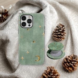 May include: Sage green phone case and matching PopSocket with gold star and crescent moon accents. The case and PopSocket have a textured appearance. Two pinecones are also in the image.