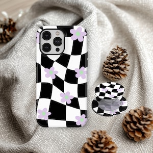 Könnte beinhalten: Schwarz-weiß karierte Handyhülle mit hellvioletten Blumenakzenten. Ein passender Handyhalter ist ebenfalls sichtbar. Die Handyhülle liegt auf einer grauen Oberfläche mit Tannenzapfen.