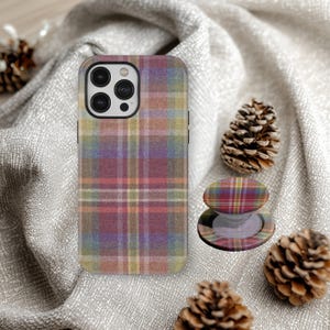 May include: A phone case and phone grip featuring a colourful plaid design in red, purple, green, and yellow. The phone case is on a grey surface with pine cones.