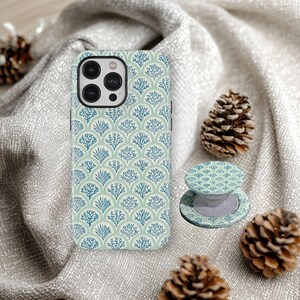 Puede incluir: Una funda y un soporte para teléfono con un patrón de coral azul y verde a juego. La funda del teléfono está sobre una tela gris con piñas.