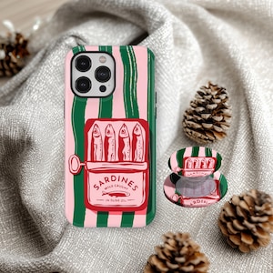 Peut inclure: Coque de téléphone à rayures roses et vertes avec un motif de boîte de sardines. La boîte rouge porte l'inscription "Sardines Wild Caught in Olive Oil" et présente quatre illustrations de poissons. Un support de téléphone assorti est également visible.