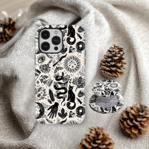May include: A smartphone case and a matching circular phone grip featuring a cream background with a black ink-style pattern of cats, snakes, suns, moons, crystals, hands, eyes, and botanical elements arranged in a dense, repeating design.