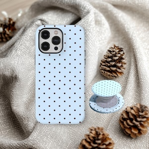 Puede incluir: Una funda para smartphone de color azul claro con un patrón repetitivo de pequeños puntos de color marrón oscuro, acompañada de un soporte circular plegable para teléfono que muestra el mismo diseño de puntos.