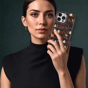 Puede incluir: Funda de tel&eacute;fono inteligente con un dise&ntilde;o de estanter&iacute;a, libros, una luna creciente e ilustraciones de fantasmas. La funda tiene un fondo oscuro con lomos de libros de tonos c&aacute;lidos y luces brillantes.