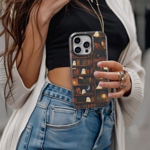 Puede incluir: Funda transparente para tel&eacute;fono con un dise&ntilde;o de estanter&iacute;a espeluznante e ilustraciones de fantasmas peque&ntilde;os. La funda tiene un fondo oscuro similar a la madera con libros, una luna y una linterna. La funda est&aacute; dise&ntilde;ada para un tel&eacute;fono inteligente.