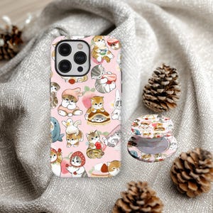 Könnte beinhalten: Rosa Handyhülle und passender Pop-Socket mit einem sich wiederholenden Muster von Cartoon-Katzen in verschiedenen Posen und Outfits. Die Hülle ist für ein Smartphone konzipiert, der Pop-Socket ist rund und befestigt.