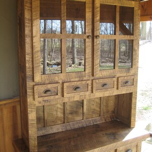 May include: A rustic wooden hutch with glass doors and drawers. The hutch has a distressed finish and is made of reclaimed wood. It features a top shelf with glass doors and a lower shelf with drawers. The hutch is ideal for storing and displaying dishes, glassware, and other kitchen items.