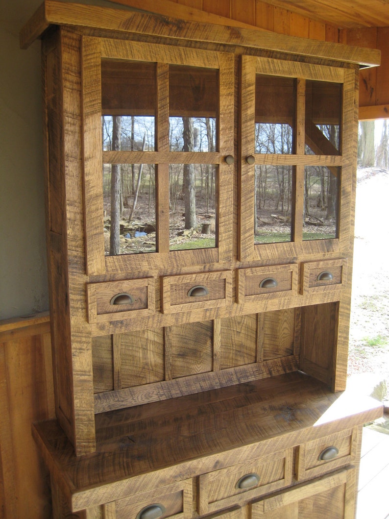May include: A rustic wooden hutch with glass doors and drawers. The hutch has a distressed finish and is made of reclaimed wood. It features a top shelf with glass doors and a lower shelf with drawers. The hutch is ideal for storing and displaying dishes, glassware, and other kitchen items.