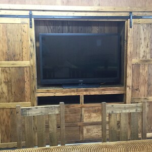 May include: A rustic wooden entertainment unit with sliding barn doors, a flat screen TV, and shelves for storage. The doors are made of reclaimed wood with a natural finish.