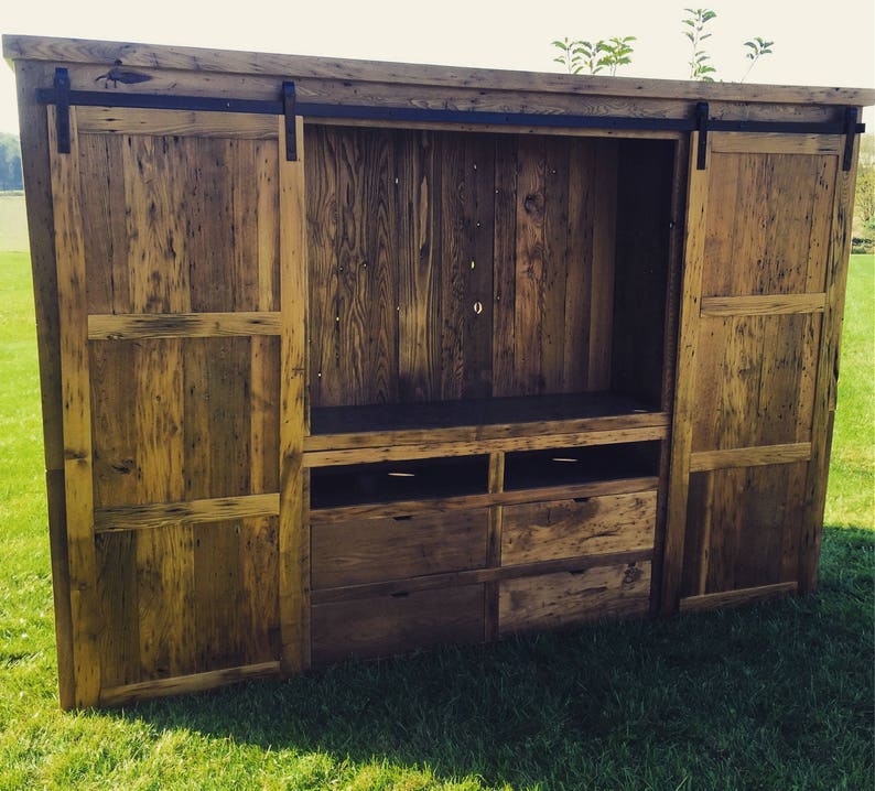 May include: A rustic wooden entertainment centre with sliding barn doors and drawers. The cabinet is made of reclaimed wood and has a natural finish.