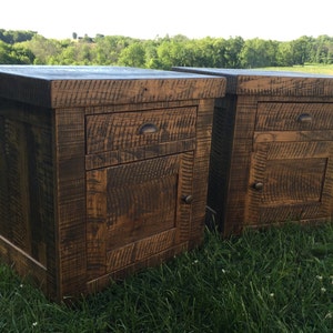 May include: Two rustic wooden nightstands with a drawer and a door. The nightstands are made of reclaimed wood and have a dark brown finish.