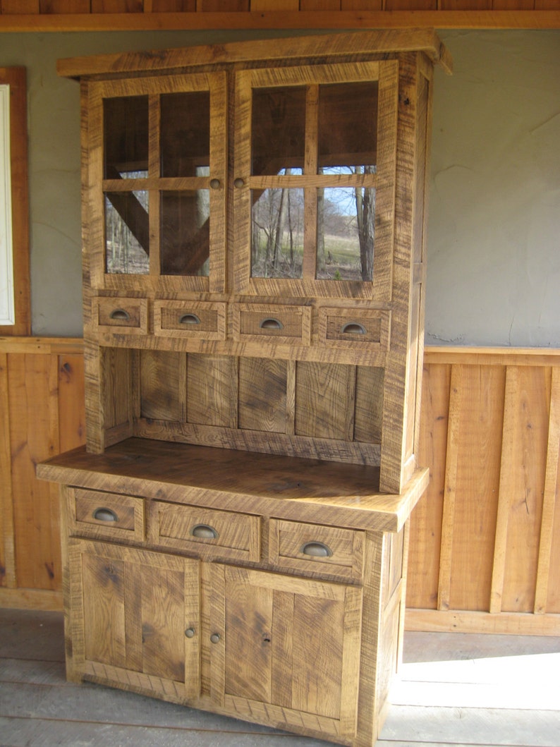 May include: A rustic wooden hutch with glass doors and drawers. The hutch has a distressed finish and is made of reclaimed wood. It features a top cabinet with glass doors and a bottom cabinet with drawers and doors.