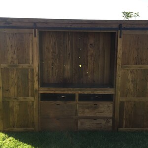 May include: A rustic wooden entertainment unit with sliding barn doors, a large open shelf, and four drawers. The doors and shelves are made of reclaimed wood with a natural finish.