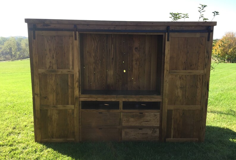 May include: A rustic wooden entertainment unit with sliding barn doors, a large open shelf, and four drawers. The doors and shelves are made of reclaimed wood with a natural finish.
