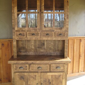 May include: A rustic wooden hutch with glass doors and drawers. The hutch has a distressed finish and is made of reclaimed wood. It features a top cabinet with glass doors and a bottom cabinet with drawers and doors.