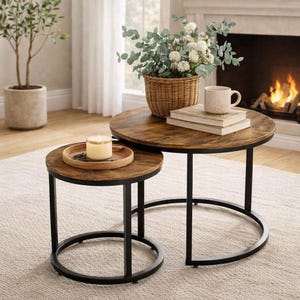 Puede incluir: Dos mesas de centro redondas con tapas de madera y marcos de metal negro. La mesa más grande tiene una cesta de mimbre con vegetación, una taza y libros. La mesa más pequeña tiene una bandeja de madera con una vela.