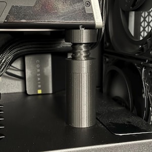 May include: A computer case interior with a graphics card supported by a cylindrical stand. The graphics card is labeled "750 XT". Black fans and cables are visible, along with a Corsair power supply. The case has a black, textured finish.