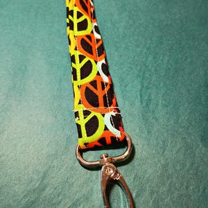 May include: A colorful lanyard featuring a peace sign pattern in orange, yellow, and white on a black background. The lanyard has a silver-colored metal clasp.
