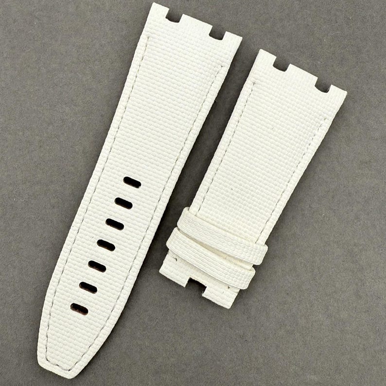 May include: Two-piece white watch strap with a textured surface. The strap has a rectangular shape with rounded edges and a series of holes for adjustment. The stitching is white, and the strap is designed to attach to a watch face.